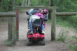 picture of a woman on a mobility scooter trying to get under a barrier constructed to prevent vehicles and bicycles from entering the path