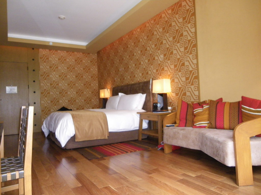 Hotel bedroom with polished floors, orange and red pillows on a couch and textured wallpaper