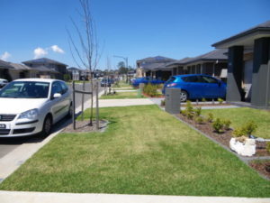 Shows the street of a new housing development with driveways for cars but no footpath for people