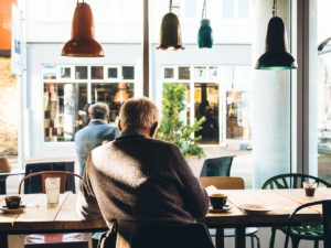 An older man sits with his back to the camera in a cafe. Urban planning for dementia allows people to get out and about.