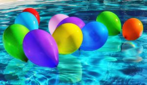 10 balloons of different colours float on the surface of a swimming pool. Transgender recreation and inclusion..