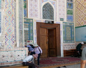 People at the mosque door taking off their shoes. One person is sitting. Making mosques accessible. 