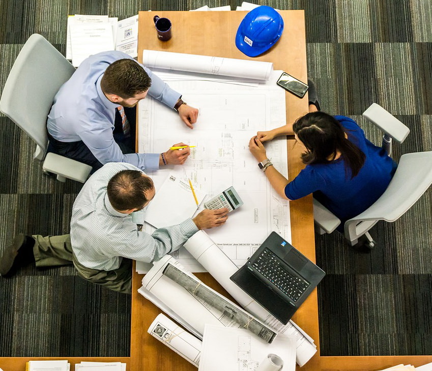 aerial view of three people at a desk looking at a set of construction drawings