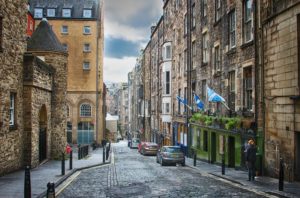 A street scene. Cobbled roadway between five and six storey heritage buildings with Scottish flags flying