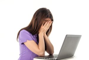A young woman sits at a desk with her laptop open. She has her face covered by her hands and is indicating distress. WCAG guidelines for people who haven't read them.