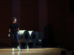 Liz Jackson on stage wearing black and using a purple cane. Beauty - the 8th principle of universal design.