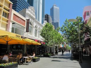 long view of a Perth city mall with shops and cafes under awnings and trees for shade. Tall buildings are in the background. Urban planning.