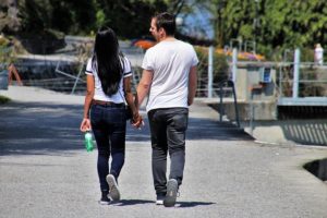 A young woman and young man are walking on a wide concrete path. They are wearing white T shirts and jeans.