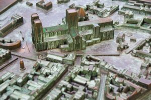 A metal model showing a town layout in relief with Braille on buildings and streets. There is a church and lots of houses and a town square represented.