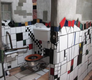 Public toilet in Kawakawa New Zealand. It has large mosaic tiles all at different angles. The toilet seat is timber