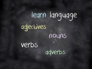 A blackboard with words: learn, language, adjectives, nouns, verbs, adverbs written in chalk