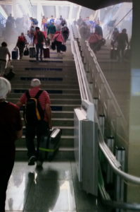 People are carrying heavy luggage up 56 steps at a train station. A platform lift remains folded at the bottom of the steps.
