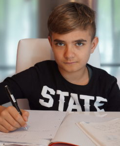 A boy sits at a desk, pen in hand ready to write on the paper.