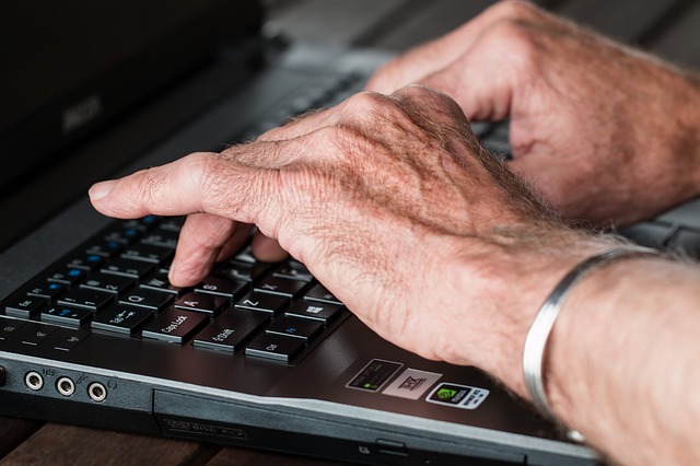 Two hands of an older person are poised above the keyboard of a laptop computer.
