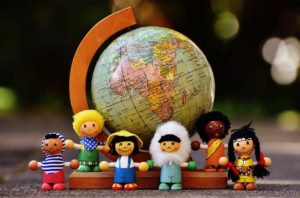 A globe atlas of the world sits on a desk and lined up in front are small dolls representing different countries