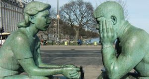 Two green statues, one a man the other a woman sit facing each other in a gesture of communicating with each other. Inclusive communication strategies.