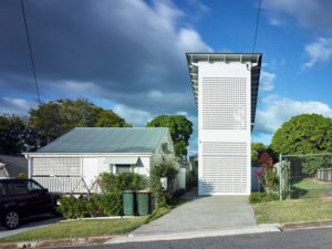 Picture of a tall long skinny house with white lattice covering. It fits into a driveway.