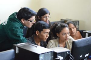 A group of five students cluster around a computer screen. They look as if they are seeing something important.