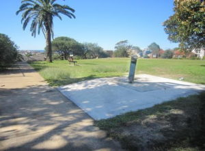 Drinking fountain has a larger concrete surround and is connected to the footpath.