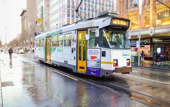 A Melbourne tram moves along a quiet street after the rain. A cyclist is in the background.