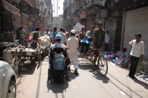 Martin Heng is in a very busy street in India. It shows donkey carts cars and bicycles with street vendors on either side.