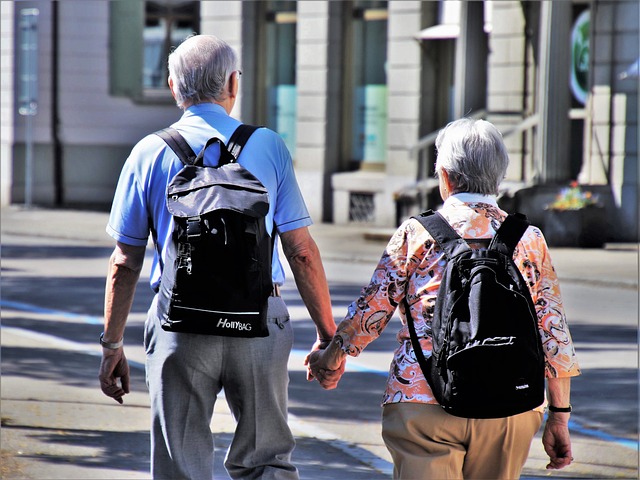 An older man and woman are walking away from the camera down a street. They are wearing backpacks and holding hands. Where do you want to live when you grow older?