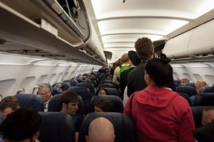 Inside the cabin of an aircraft, people are queuing in the aisle to take their seats