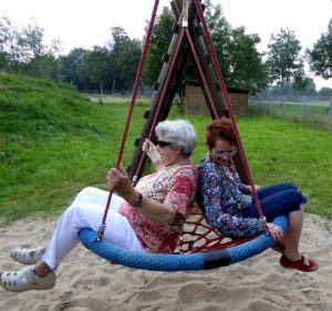 Two women sit on a bird nest swing depicting a positive image of older people.