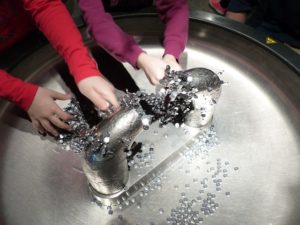 Hands of two children are over a large bowl with lots of little button magnets. They are experimenting through play.