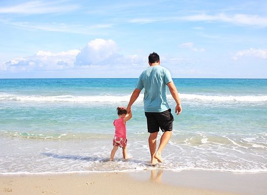 A man holds the hand of a small girl as they wade into the water on the beach. Travel and tourism.