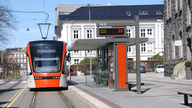 An orange tram is arriving at the light rail station.