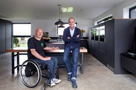 Kevin McCloud stands in the kitchen with Mark Butler who sits in a wheelchair. Grand Design as accessible design.