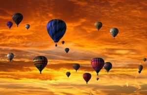 A orange-yellow sky with many coloured hot air balloons. 