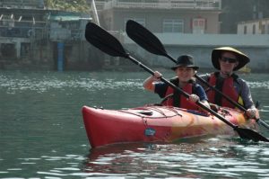 A man and boy are wearing hats and paddling in an orange kayak..
