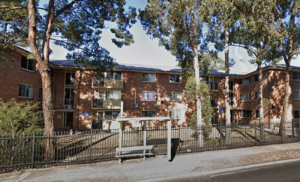 A group of red brick three storey apartments shaded by trees. 