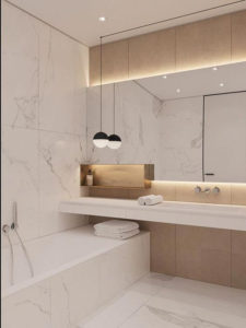 Pale marble tiles line the walls of this bathroom. There is one long shelf with a mirror behind. A bath with a hand held shower is fitted just above the bath rim.