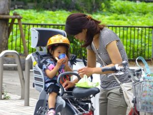 A young woman attends to a small child in a child seat on the back of the bicycle. The bike has a shopping basket.