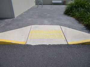 A concrete kerb ramp with yellow tactile markers on the slope.