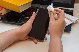 A disinfectant wipe is used to wipe over a mobile phone and computer keyboard.