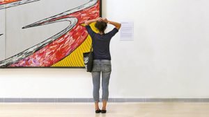 A woman standing with her back to the camera, looking towards a contemporary painting.