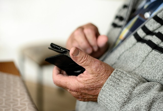 A pair of hands belonging to an older man hold a mobile phone.