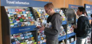 two people stand in front of racks of tourism brochures.