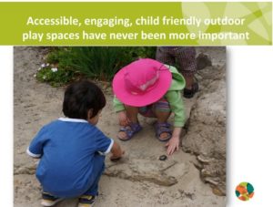 Two small children crouch down in a sandy area with large stones. Good to see creative and inclusive play.