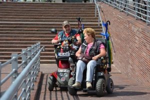 A woman in a powered wheelchair and a man in a mobility scooter enjoy the pathway.