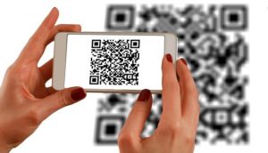 A woman holds a smartphone over a QR code. It makes for smart cities.