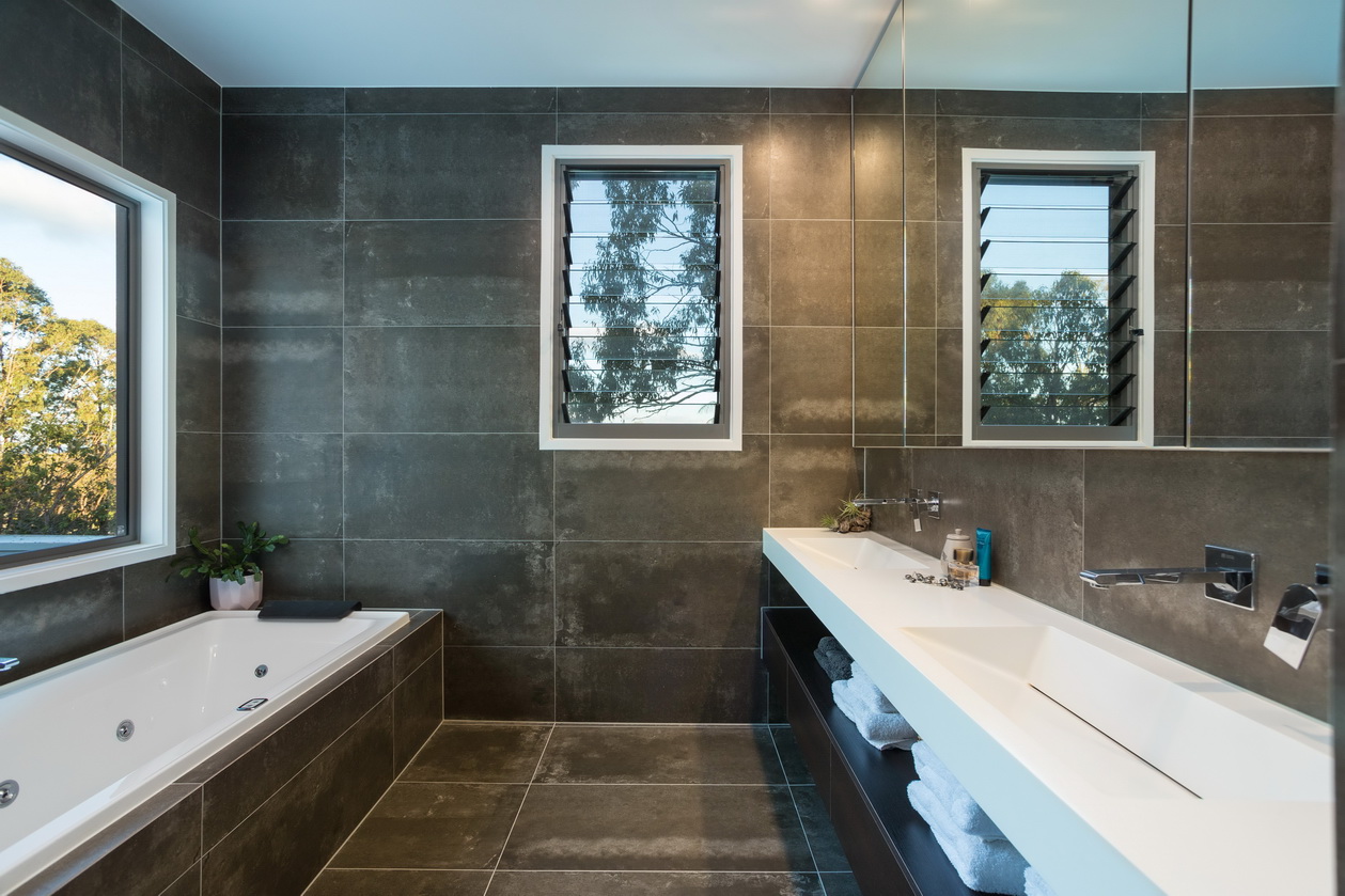 Bathroom design with dark tiles and floor and white bath and vanity bench.