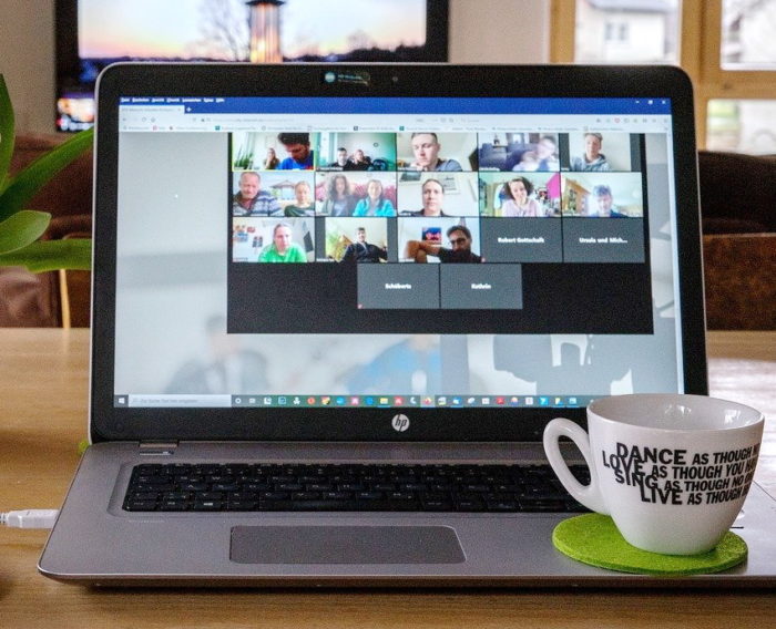 A laptop screen is open showing participants in an online meeting or hybrid event. 