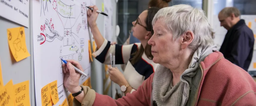 An older woman is writing something on a wall chart alongside others. 