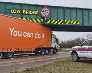 A semi-trailer is stuck under a bridge with the warning "low bridge" in upper case. 
