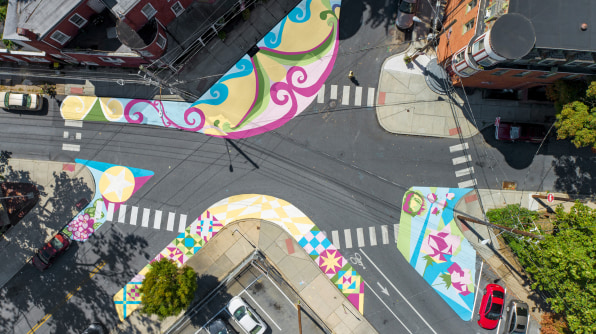 Aerial view of a street intersection showing the street art painted on the road surface. There is a mix of different brightly coloured patterns. 